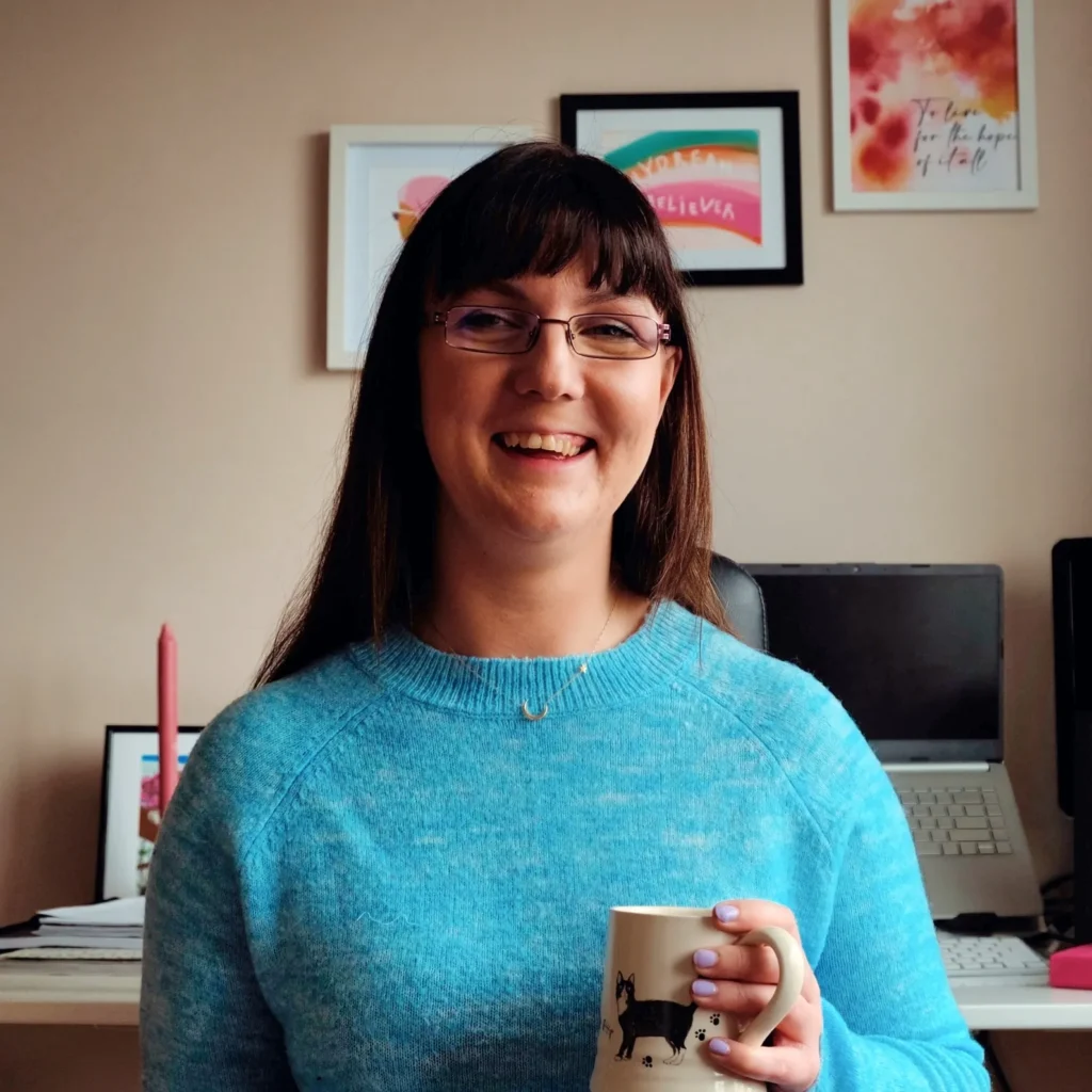 Friendly female copywriter in blue jumper working from home office with laptop and coffee mug
